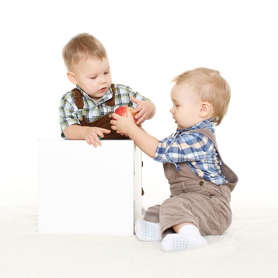 Two little boys with fresh apple sit on a white background. Healthy food.