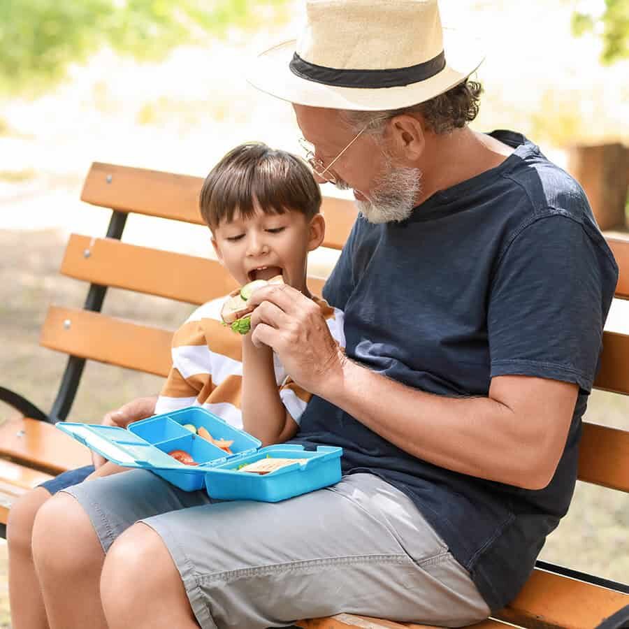 Senior man giving sandwich to his little grandson in park